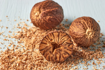 Three textured nutmegs and grated powder on a light wooden background. Spices for cooking