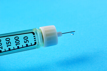 Transparent drop of insulin close-up on the tip of a syringe needle on a blue background