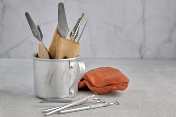 Metal mug with many sculptural tools for modeling clay and plasticine against a light workshop background