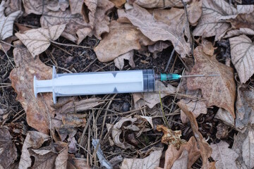 one white syringe with a needle lying on the ground and brown dry leaves in the street