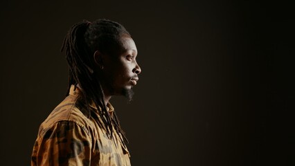 Smiling person posing in studio with black background, feeling confident wearing dreads and camo...
