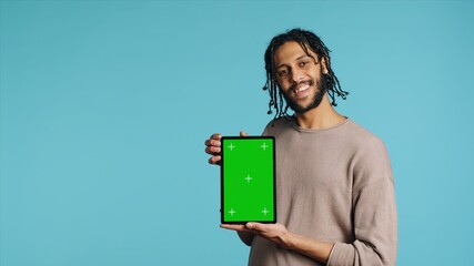 Joyful man holding green screen tablet, showing positive emotion. Upbeat person presenting chroma key device, doing recommendation, isolated over studio background, camera A