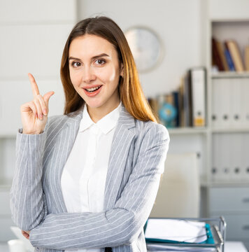 Portrait of happy business woman standing in office and pointing finger on something