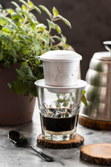 Vietnamese phin on a glass, Vietnamese coffee with condensed milk, wood stands, herbs in a pot,...