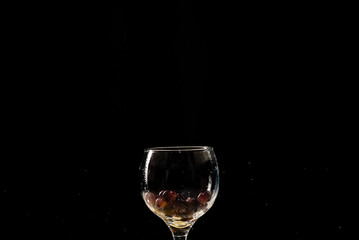 A glass of wine with water and red grapes inside.