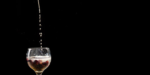 Drops of milk falling from above into glass wine glass with milk and grapes inside.