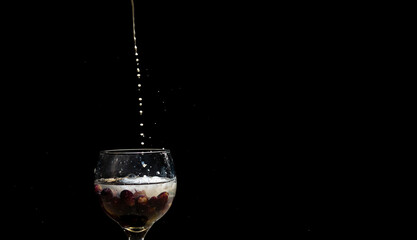 Drops of milk falling from above into glass wine glass with milk and grapes inside.