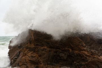 Immense waves hitting a large rock at the edge of the beach. Force of nature.
