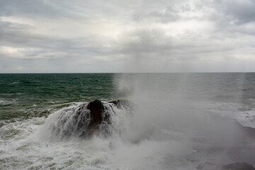 Immense waves hitting a large rock at the edge of the beach. Force of nature.
