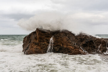 Immense waves hitting a large rock at the edge of the beach. Force of nature.