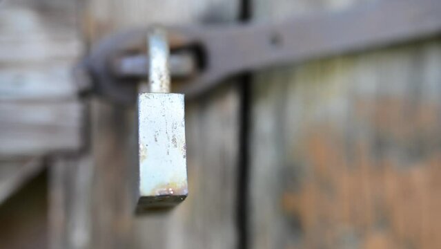 Old metal lock swinging on a rusty hinge on a dilapidated wooden shed.