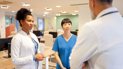 Obraz premium Medical team of one male doctor, his female African American colleague and a Japanese nurse having a meeting at the hospital dining room