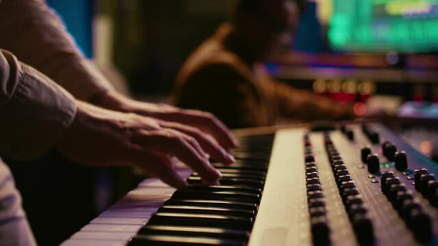 Musician composer playing midi controller synthesizer in professional studio, composing music on mixing console. Artist performing on piano electronic keyboard in control room. Camera B.