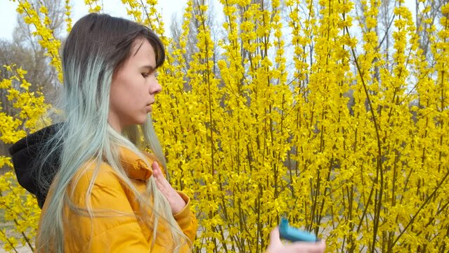 Teen with pollen reaction in park. A stylish teen girl have a reaction by the blooming tree with inhaler.