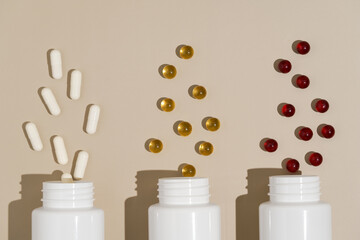 Three white mockup jars with white, yellow and red pill capsules on a beige background. The concept...
