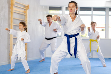 Concentrated woman practicing kata routine with husband and tween children during join family training at karate class. Concept of active lifestyle and connection between generations