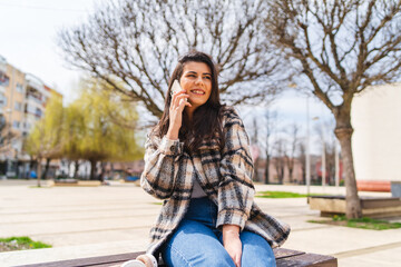 Fototapeta premium One young girl is using her phone to talk or send messages outdoors on a sunny day 