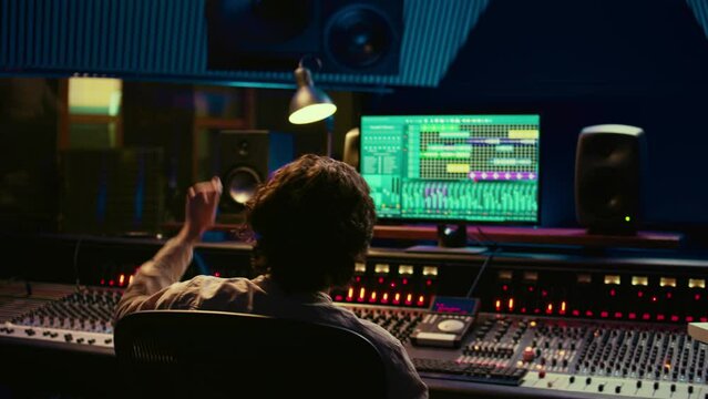 Sound engineer counting down for artist in vocal booth to start singing and producing new music, control room technical gear. Skilled audio technician operating knobs and sliders. Camera B.