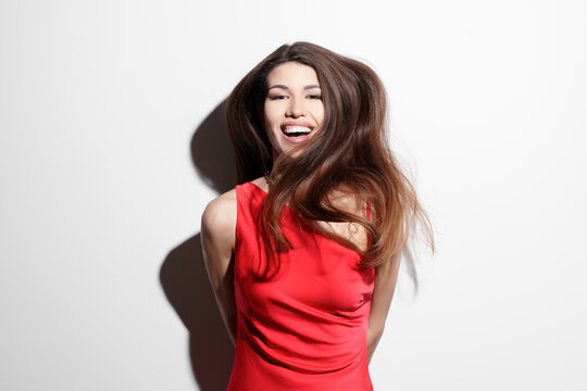 A vibrant image of a joyful young woman wearing a bright red dress against a white background, laughing with her hair flowing freely, exuding happiness and confidence.