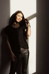 Elegant young woman with a radiant smile posing in a black outfit, bathed in natural sunlight. The...
