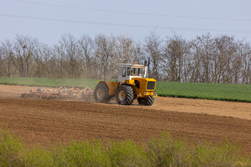 A tractor plows a field with seedbed cultivator in early spring