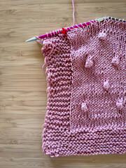 Knitting needles with pink wool on a wooden background