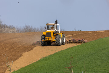 A tractor plows a field with seedbed cultivator in early spring