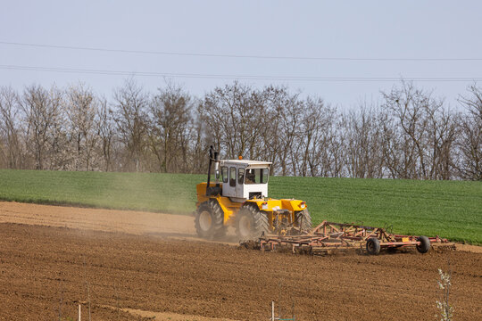 A tractor plows a field with seedbed cultivator in early spring