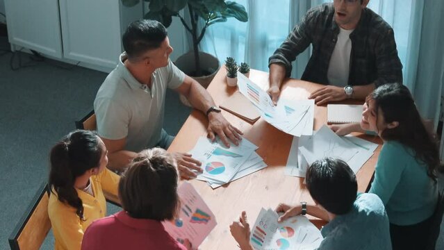 Top view of smart people throw paper and giving high five at meeting table with financial document and stock market analysis paper scattering around. Aerial view of team celebrate project. Symposium.