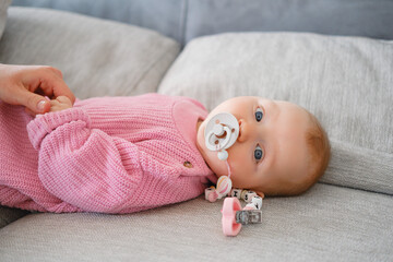 Caucasian female infant dressed in rose-colored bodysuit lying on couch. Baby girl with ginger hair...