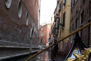 Intimate perspective from a gondola navigating a narrow, secluded canal in Venice, with historic brick buildings rising on either side. © Keifer