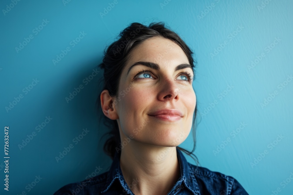 Wall mural Portrait of a young woman looking up against a blue background.