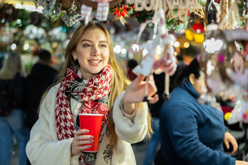 Girl is having nice time at New Years fair and shopping. Girl looks at hand-made toys in store of interior Christmas decorations.