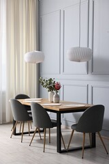 Soft chairs, table and vases with plants in stylish dining room