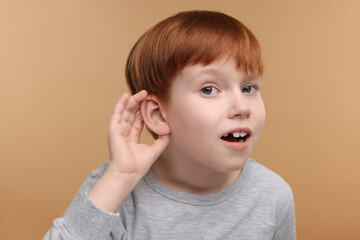 Little boy with hearing problem on pale brown background
