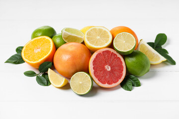 Different fresh citrus fruits and leaves on white wooden table