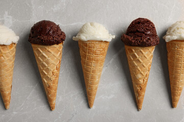 Tasty ice cream scoops in waffle cones on light marble table, flat lay