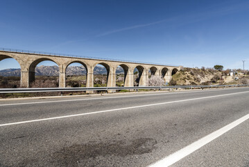 An old stone railway bridge with many arches next to a conventional road