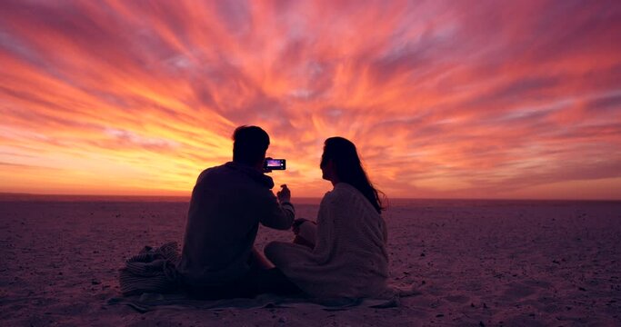 Sunset, sky and couple on beach with smartphone for photography, view and people on vacation for love and marriage. Life partner, taking pictures and memory trust and commitment with date in nature