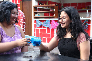 Two young brunette Latin women of 20 years old drink frosty blue cocktail with chili, celebrate by drinking alcohol