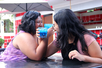 Two young brunette Latin women of 20 years old drink frosty blue cocktail with chili, celebrate by drinking alcohol