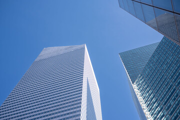Gaze upwards at the sleek geometry of New York's skyscrapers, where the contrast of glass against the blue sky epitomizes urban aspiration