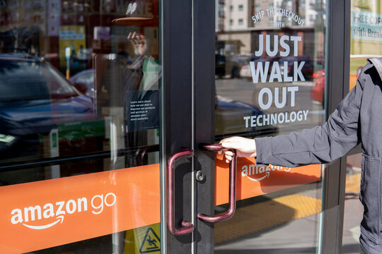 Man opens glass door of the Amazon Go store with slogan "Just Walk Out". Everett, WA, USA - March 2024