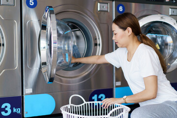 Asian Woman using self-service washing machine. Housewife putting clothes in the washing machine.