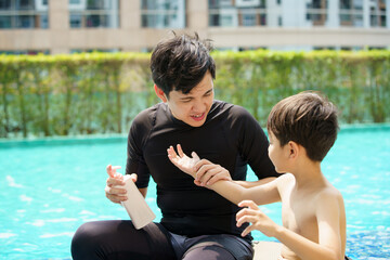 Father is applying a sun screen or sun block lotion on his son body before going to swimming in the swimming pool. Weekend vacation activities between father and son.