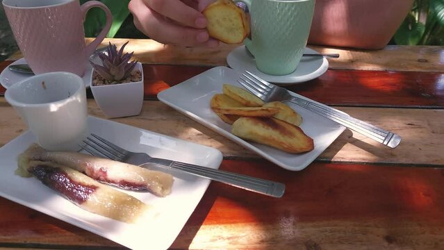 Overhead view of a traditional Filipino merienda of suman and fried kamote served with coffee with partial view of a person eating