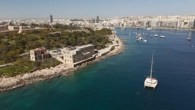 An aerial view of Maneol Island in Marsamxett Harbour, Malta. Taken at on a sunny morning with the resort town of Sliema in the background. Flying left to right around the island