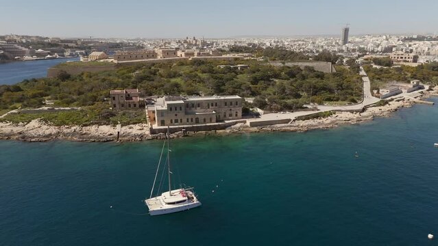 An aerial view of Maneol Island in Marsamxett Harbour, Malta. Taken at on a sunny morning with the resort town of Sliema in the background. Flying right to left around the island