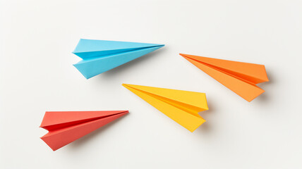 Three colorful paper airplanes on a white surface, in blue, orange, and yellow.