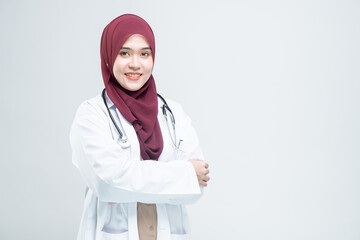 Happy beautiful asian Muslim woman doctor in medical coat standing with crossed arms, and with a smiley face ready to serve, on white background.